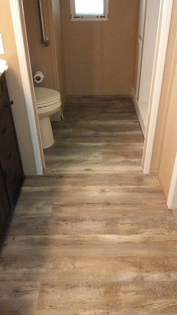 Narrow hallway with wood-look flooring leading to a small bathroom with a toilet and window.