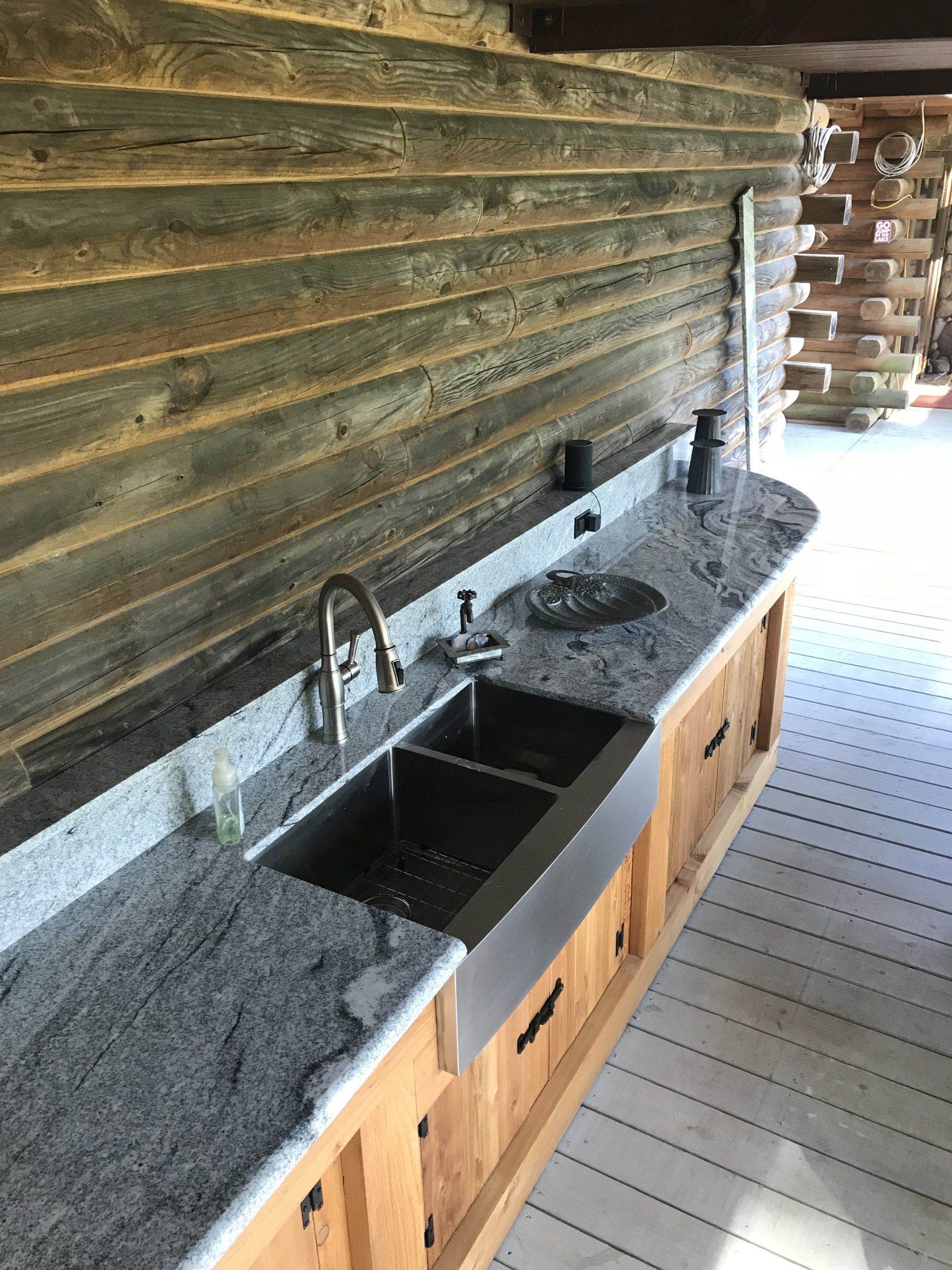 Outdoor kitchen counter with granite sink, faucet, and wooden cabinetry under a covered patio