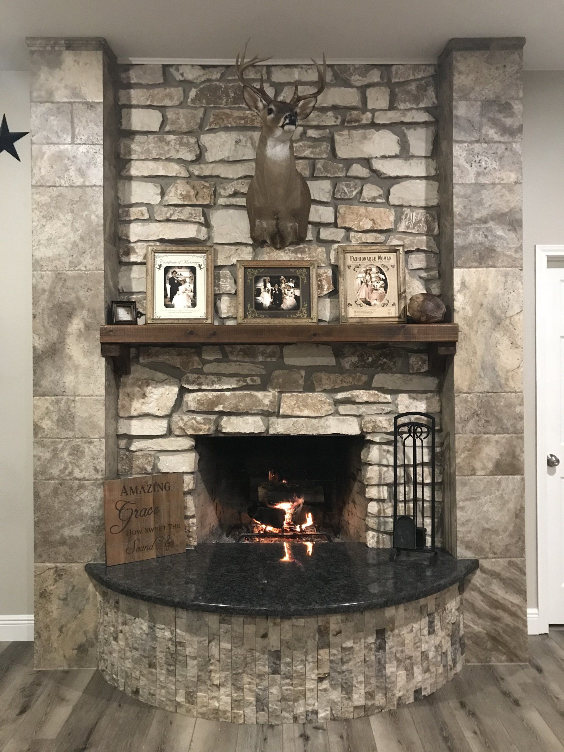 Stone fireplace with arched firebox, framed photos on mantel, and a lit fire inside.