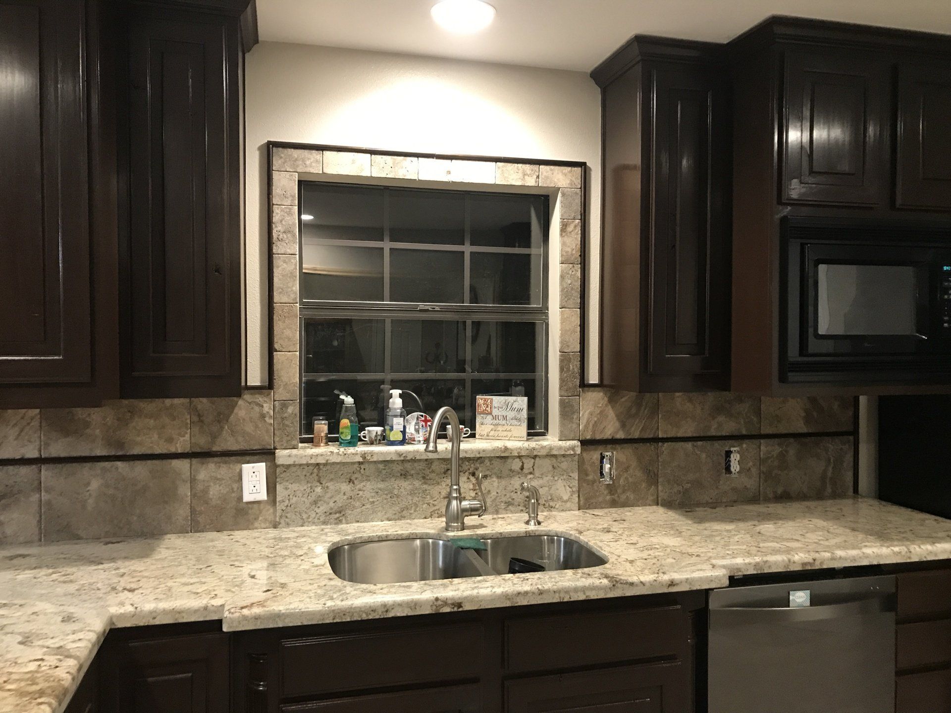 Dark kitchen with granite counters, dark wood cabinets, a window above the sink, and a dishwasher.