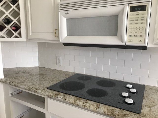Modern kitchen counter with granite top, black cooktop, microwave above, and white subway tile backsplash