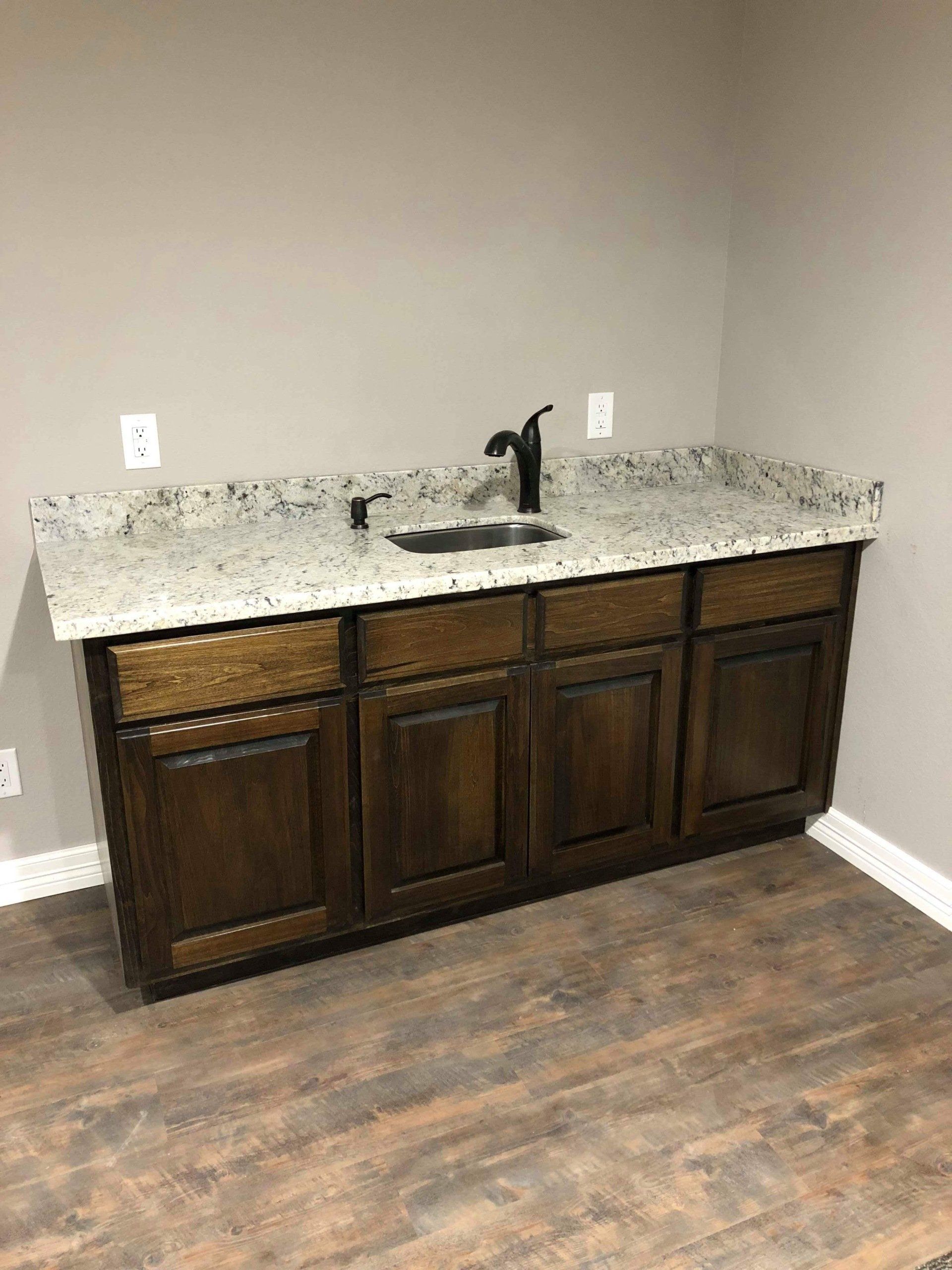 Empty bathroom vanity with dark cabinets, speckled granite countertop, and black faucet against beige walls