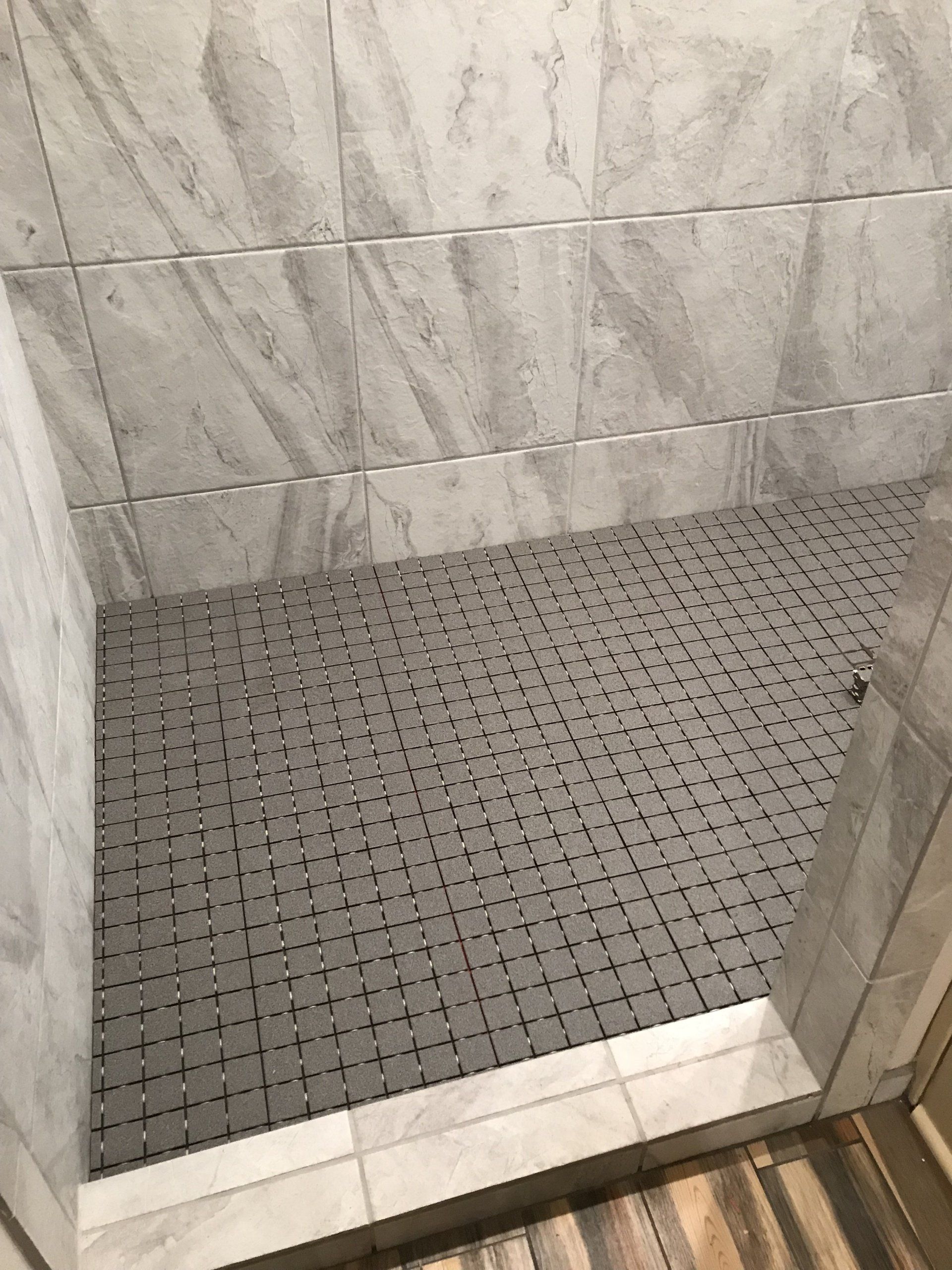 Small tiled shower stall with gray mosaic floor and white marble-look wall tiles.