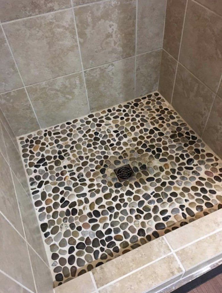 Tiled shower floor with pebble mosaic and center drain, beige wall tiles around it
