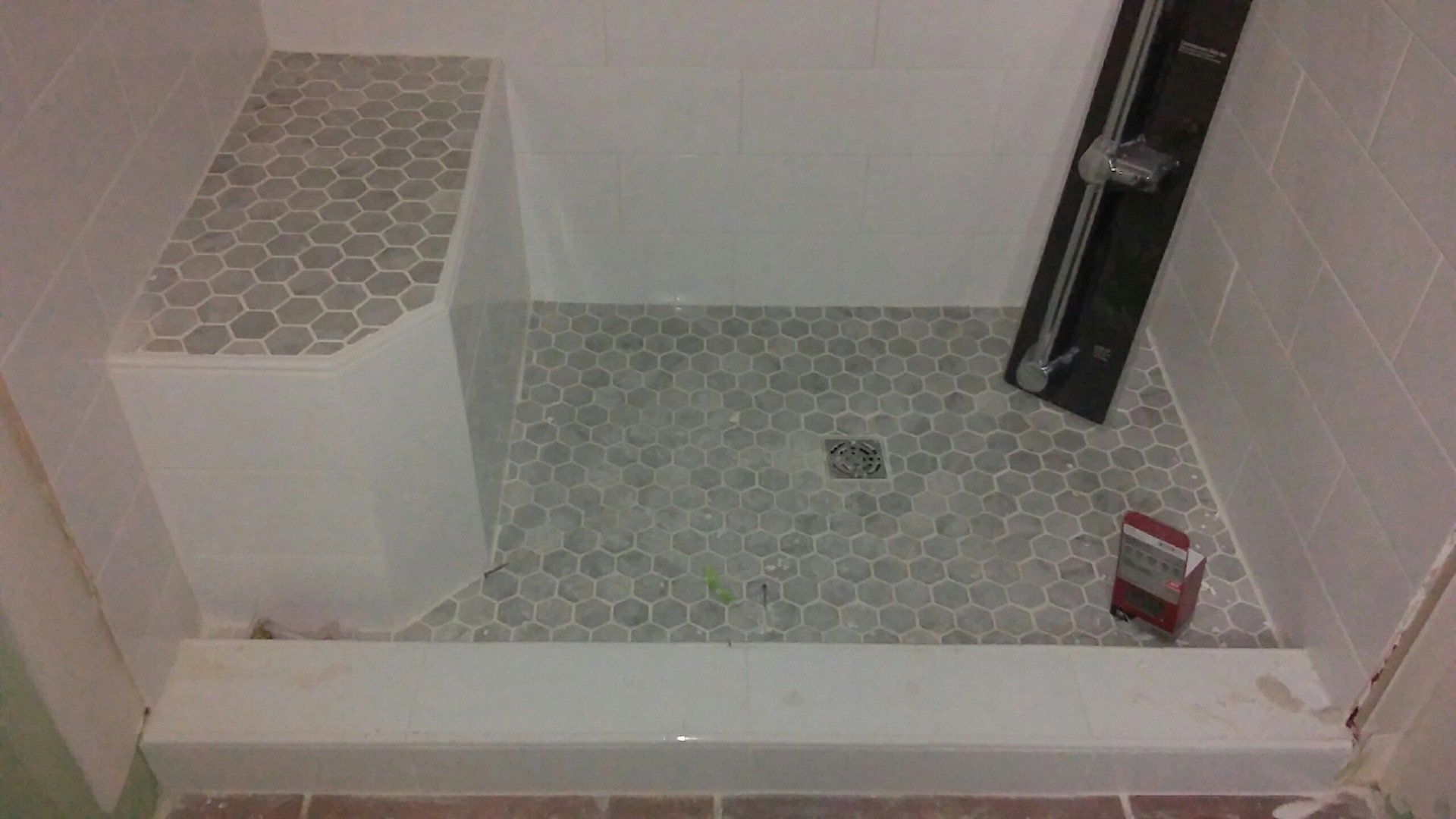 Small tiled shower stall with a raised step, white bench, and a red shampoo bottle on the floor.