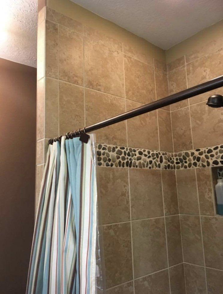 Shower stall with beige tile walls, decorative pebble border, and a black curtain rod with striped curtain