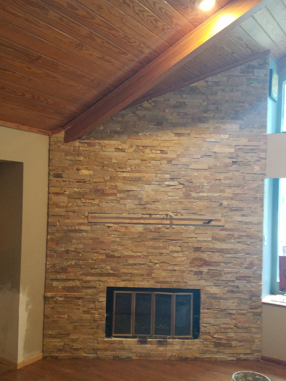 Stone fireplace beneath a slanted wood ceiling, with a window on the right