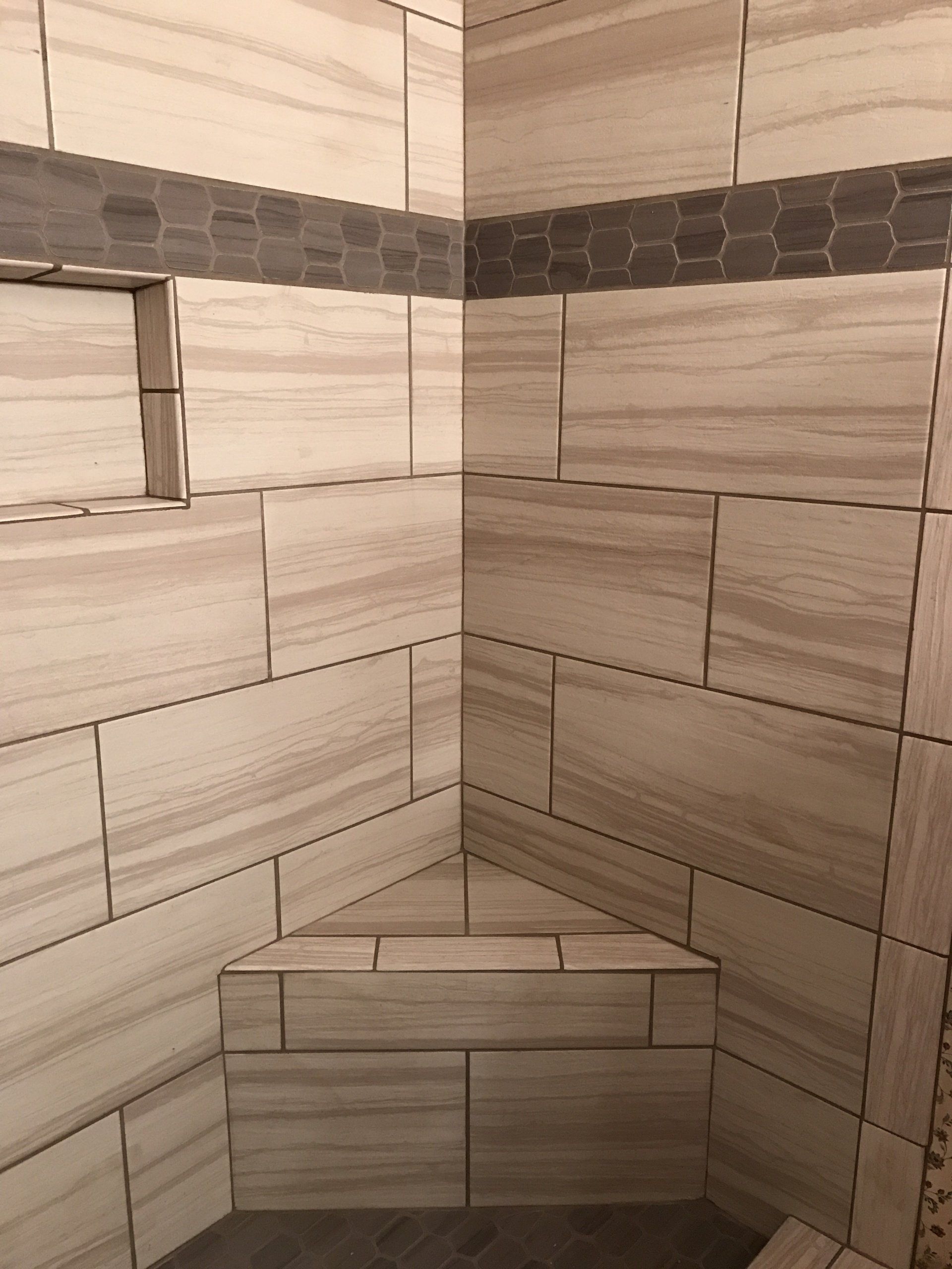 Tiled shower corner with a built-in bench and beige-gray wall tiles