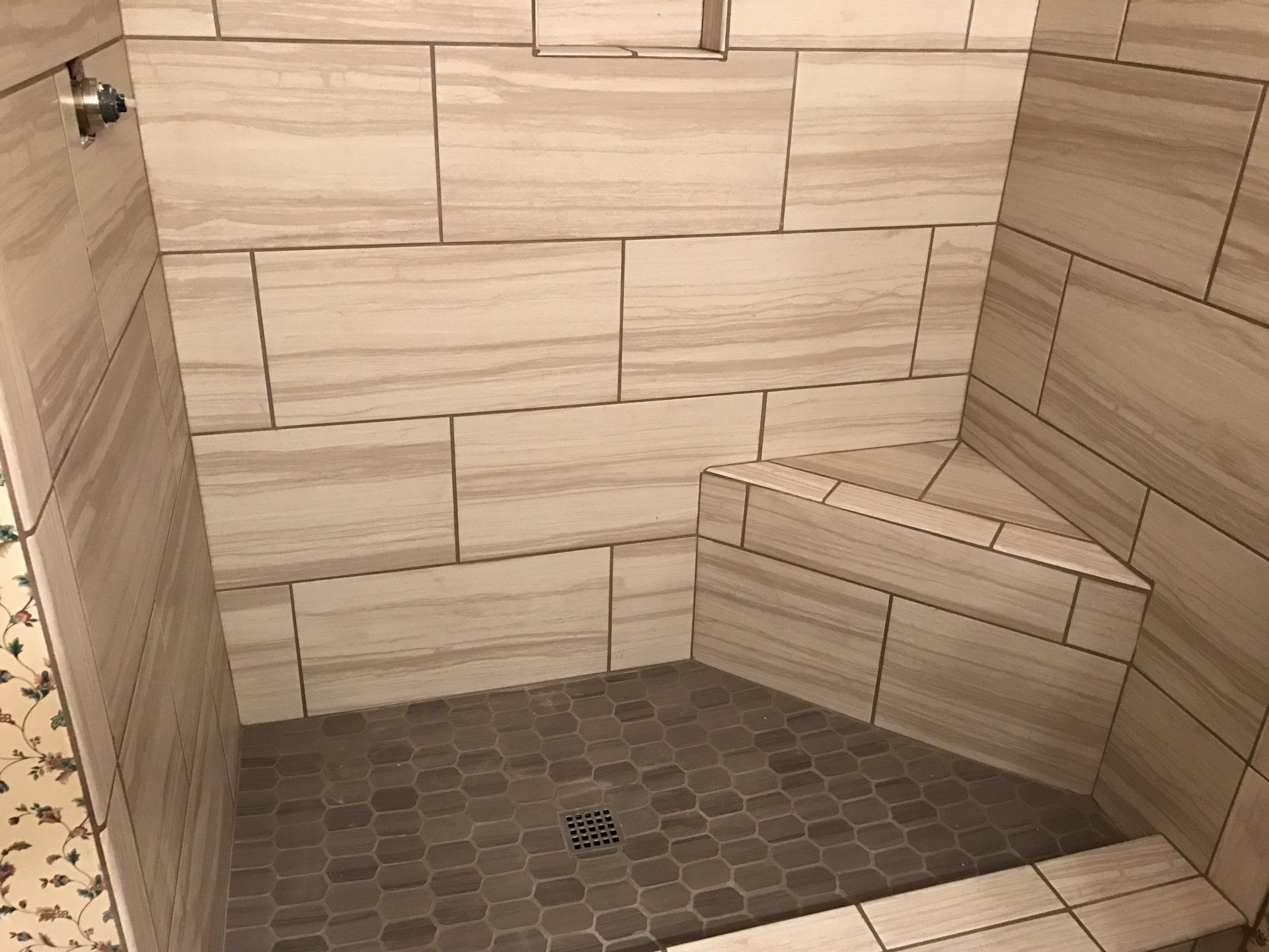 Empty tiled shower with built-in bench and hexagonal floor drain.