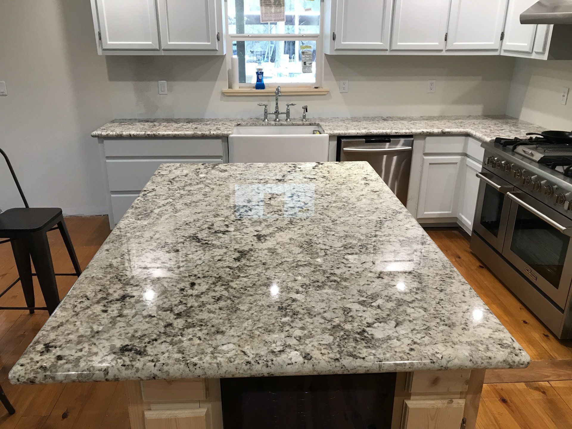 Kitchen with large granite island, white cabinets, stainless stove, and window over the sink.