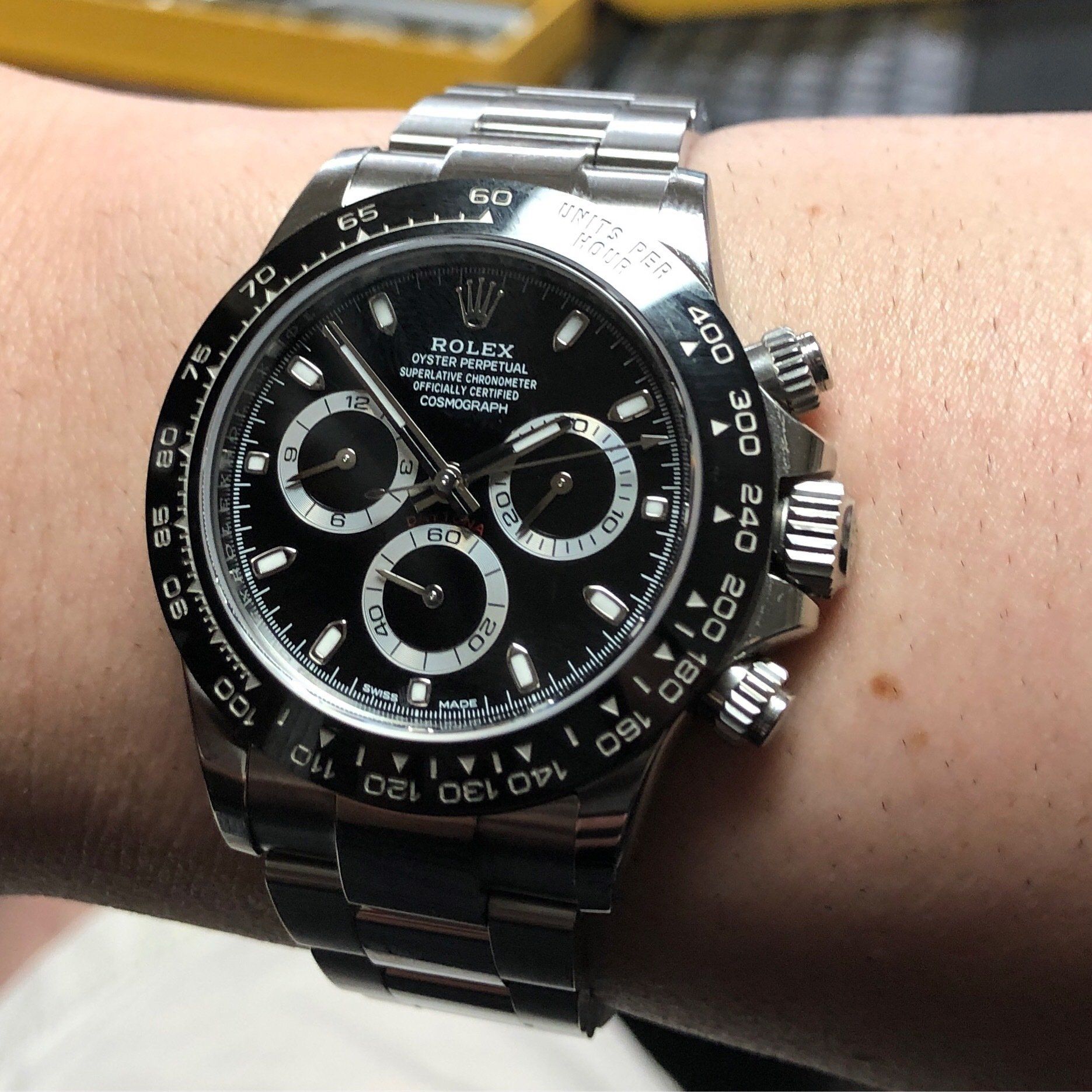 Rolex Daytona wristwatch on a wrist, black dial with white sub-dials, silver bracelet.