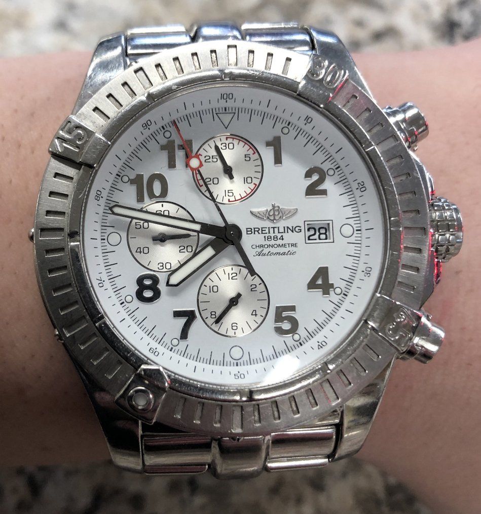 Silver Breitling Chrono Avenger watch on a wrist with white face, black hands, and silver bezel.