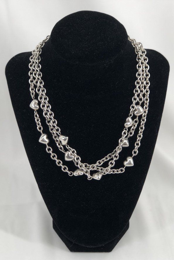 Three-strand silver necklace with heart-shaped charms displayed on a black jewelry stand.