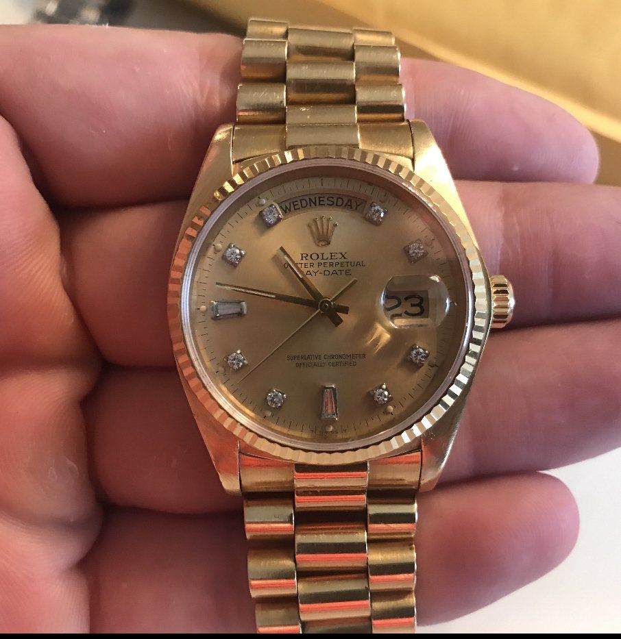 Gold Rolex Day-Date watch with diamond hour markers, held in a hand.