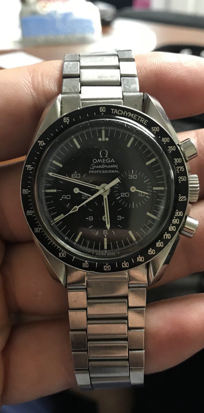 Close-up of a silver Omega Speedmaster watch on a wrist, with a black face and a metal band.