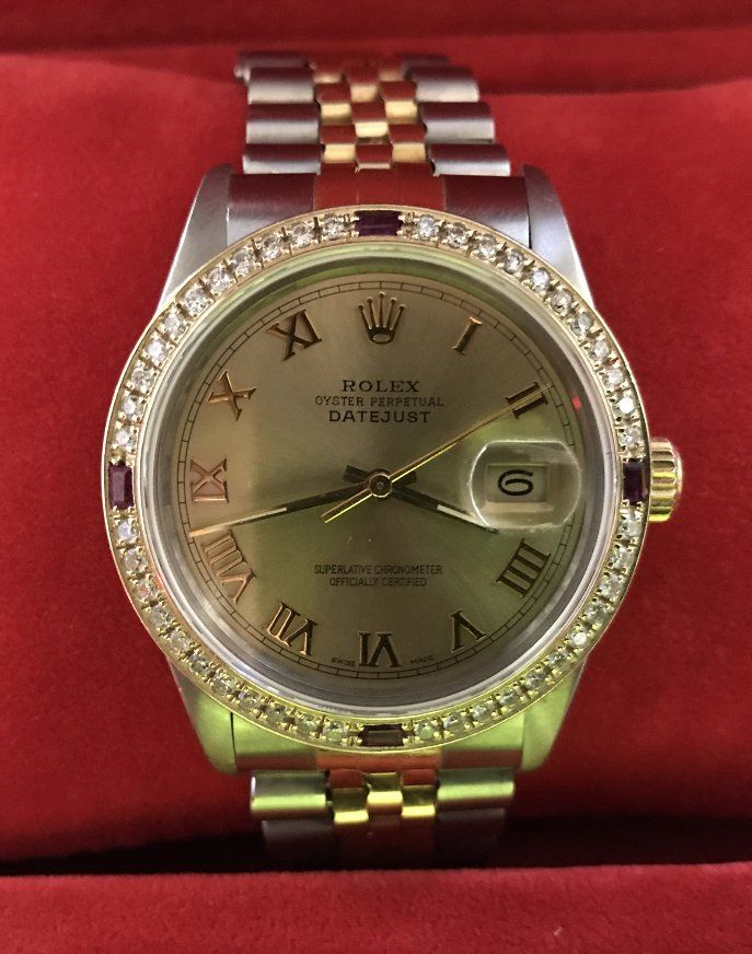 Rolex Datejust watch with diamond and ruby bezel, gold and stainless steel band, on a red background.