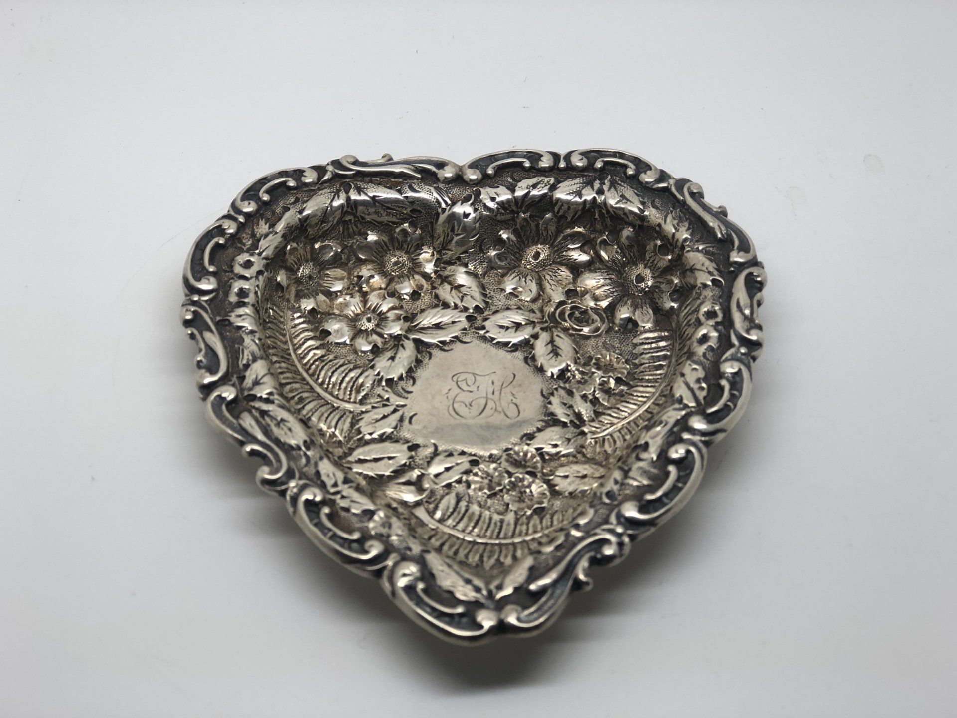 Silver heart-shaped dish with ornate floral and scroll detailing.