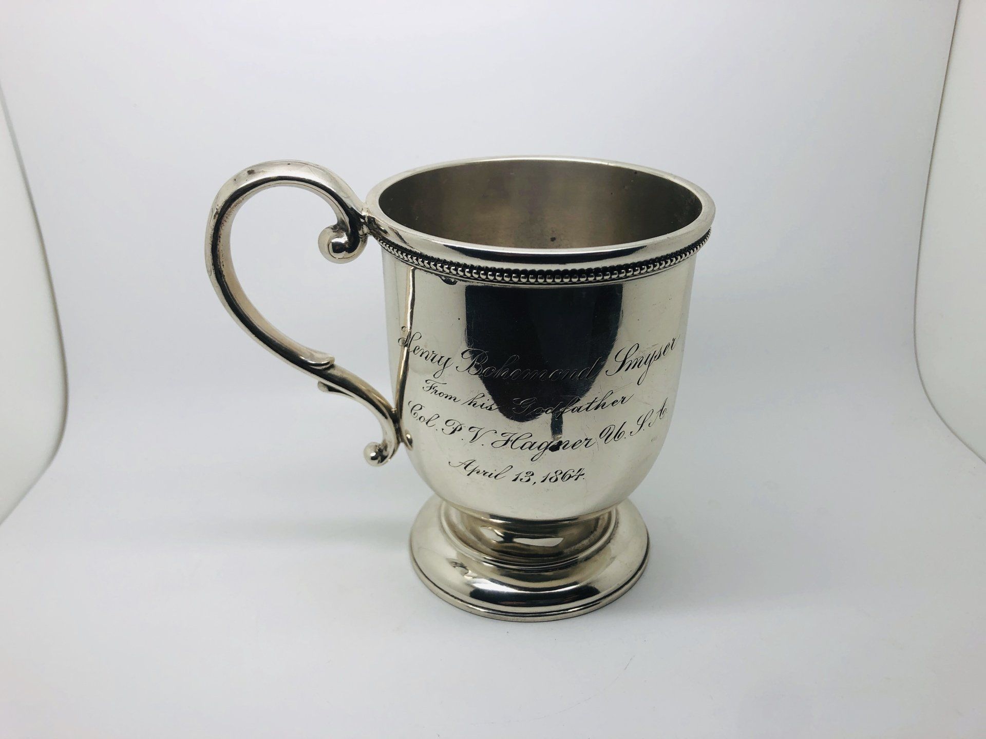Silver-colored cup with handle and ornate rim, on a white surface.