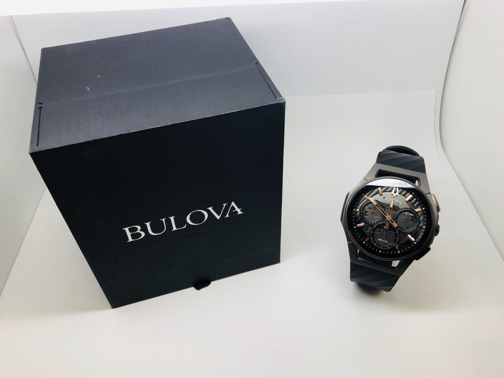 Black Bulova watch beside a black box with the Bulova logo on a white surface.