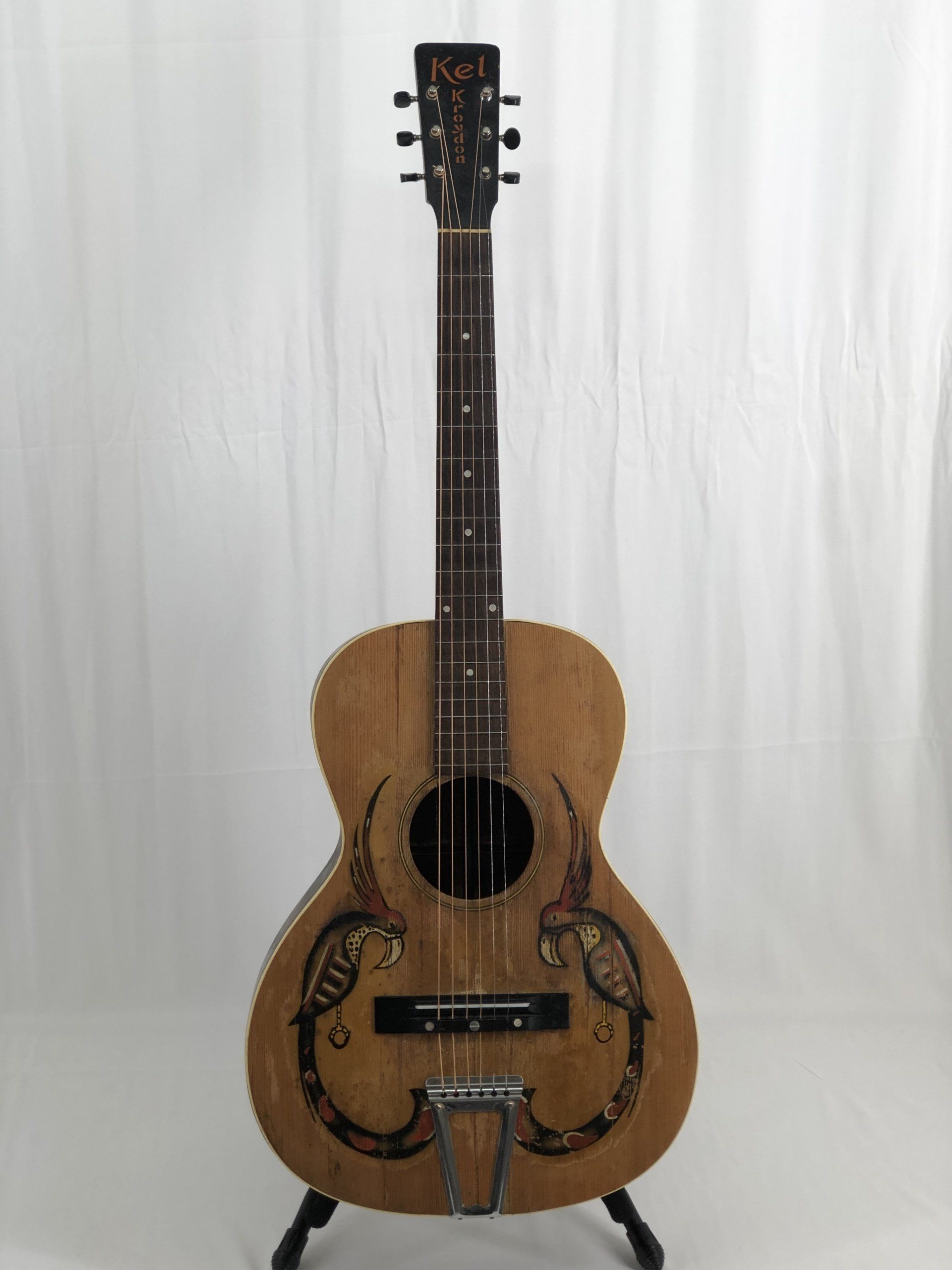 Acoustic guitar with decorative art on the body, on a black stand.