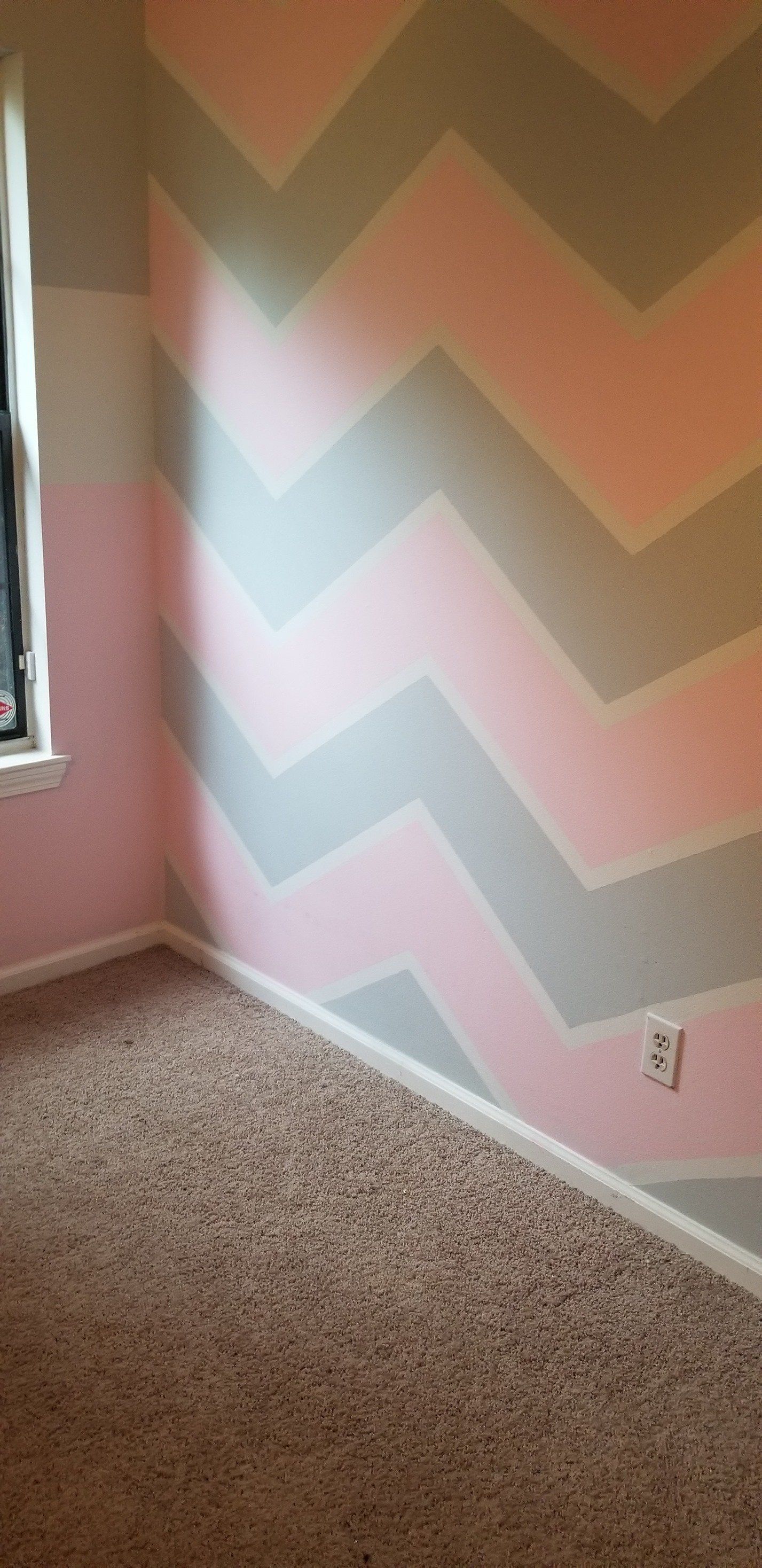 A bedroom with pink and gray chevron walls and a window.
