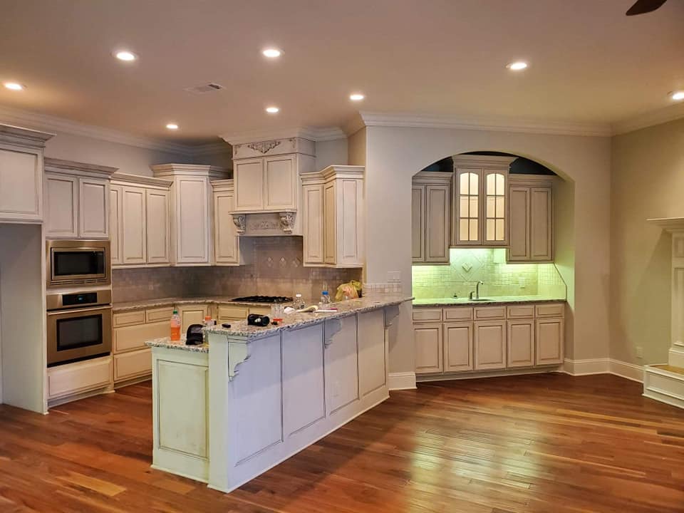 An empty kitchen with white cabinets and hardwood floors.