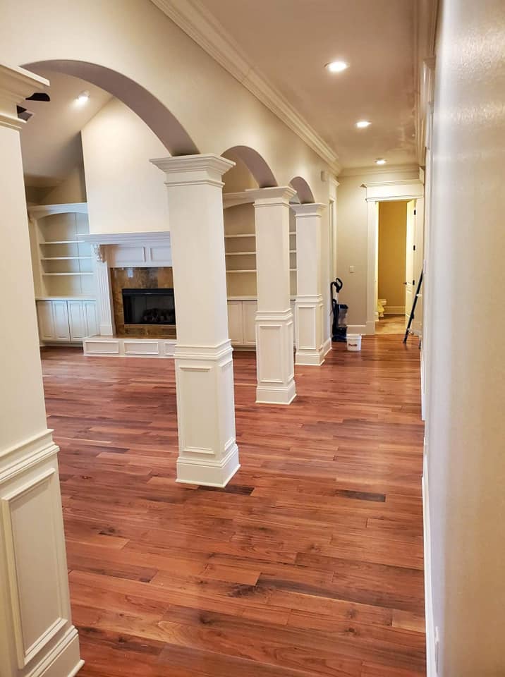 A hallway in a house with hardwood floors and white columns.