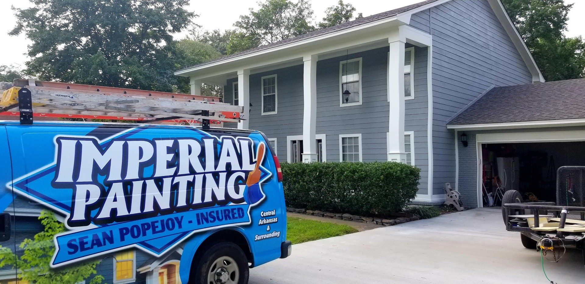 A blue imperial painting truck is parked in front of a house.