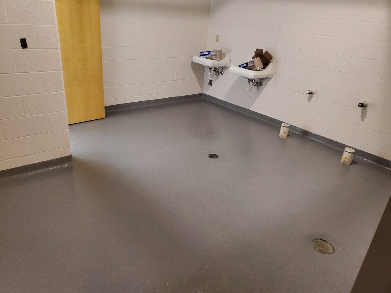 A bathroom with two sinks on the wall and a drain on the floor.