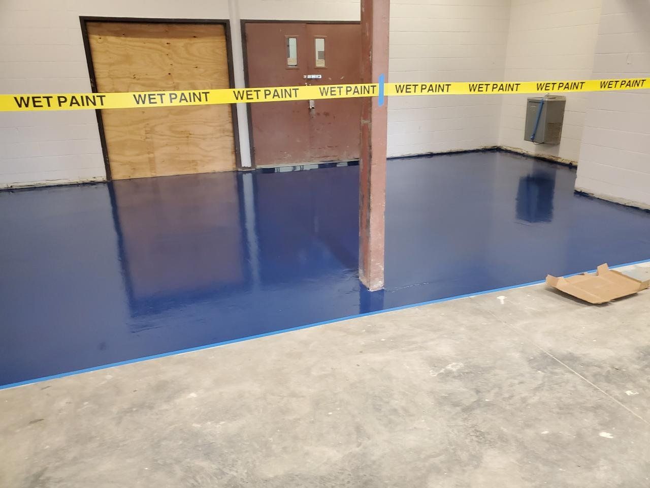A room with a blue floor and a yellow tape that says wet paint.