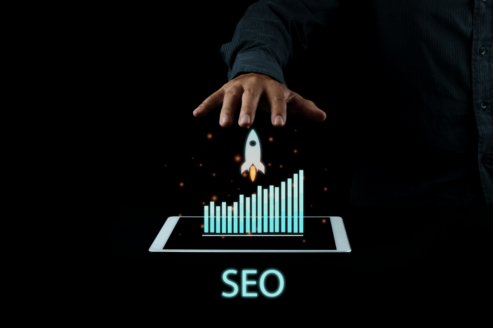 Hand on top of a rocket, a bar graph, a tablet and the word SEO