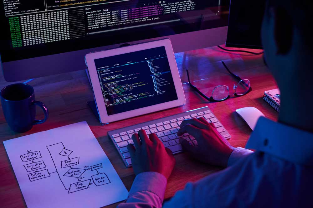 A man typing and looking at a tablet and desktop monitor.