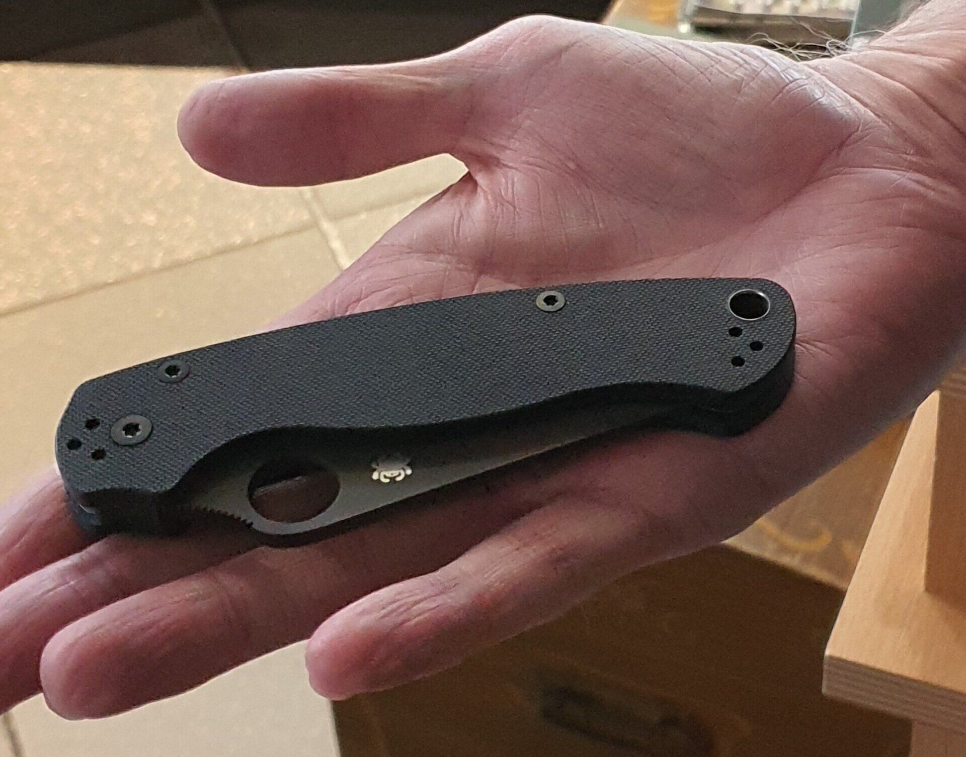 Hand hält ein schwarzes Klappmesser mit strukturiertem Griff.