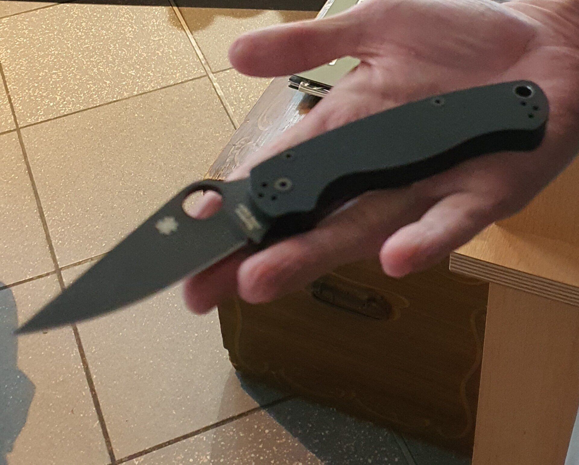 Eine Hand hält ein schwarzes Klappmesser mit einer gebogenen Klinge und einem runden Loch in der Klinge.