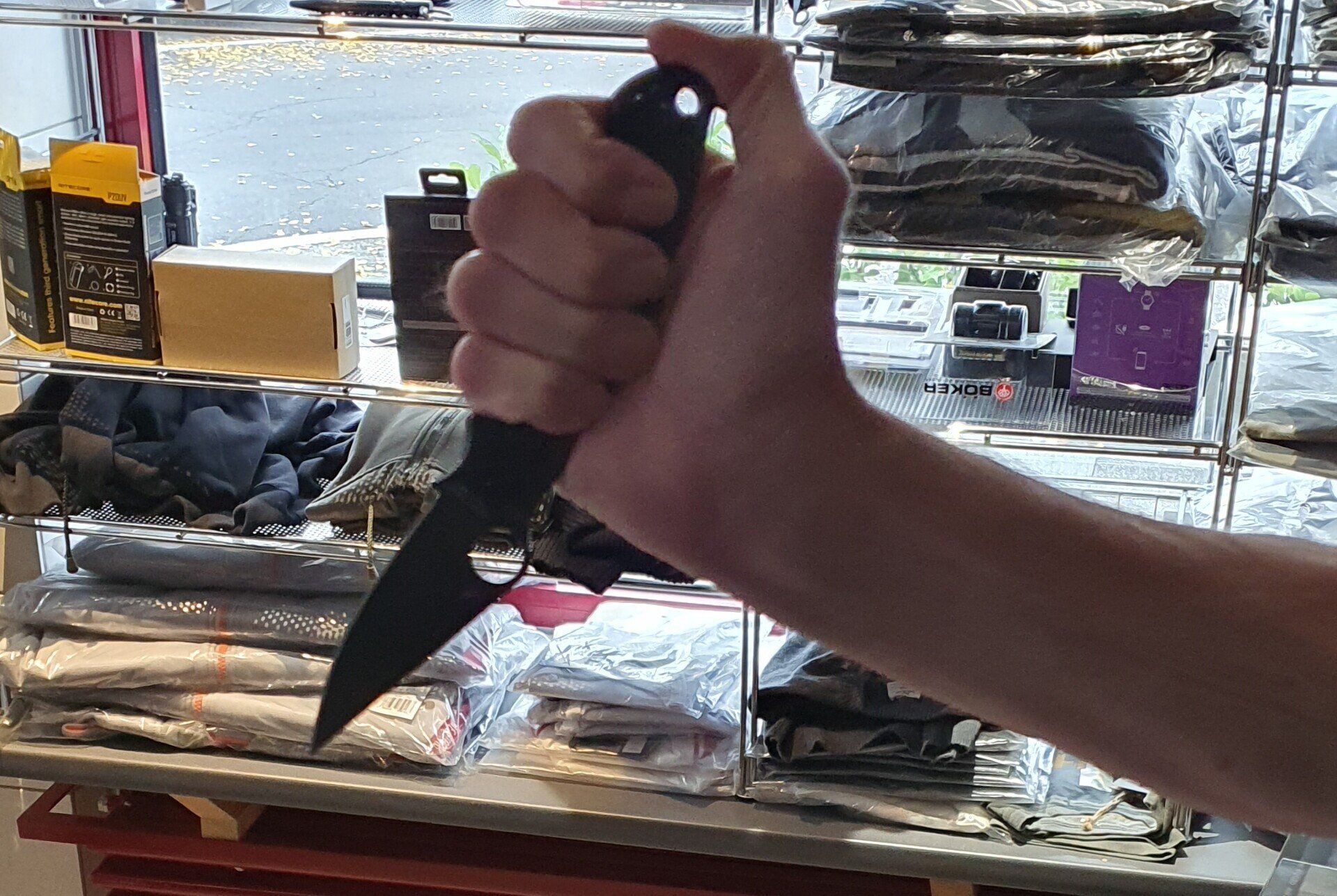 Person hält ein schwarzes Messer. Die Hand umschließt den Griff. Die Klinge zeigt nach unten rechts.