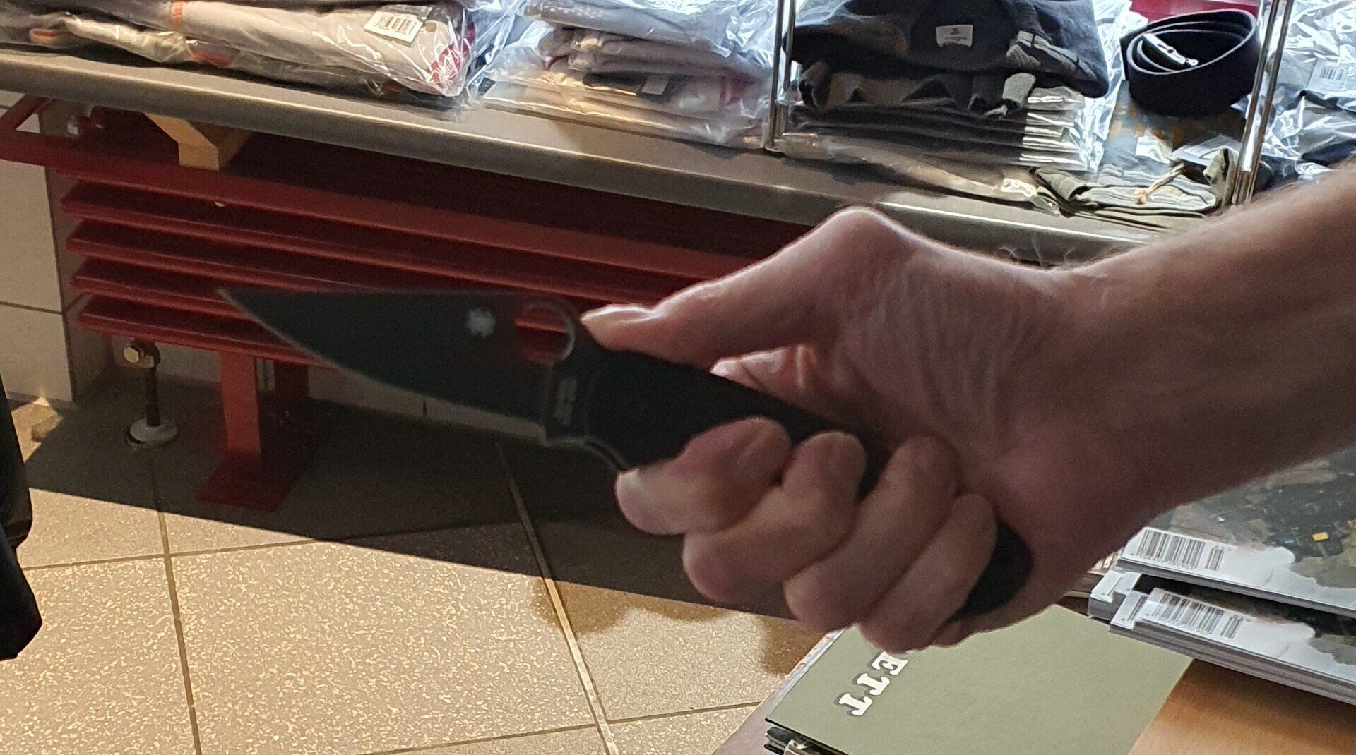 Hand hält ein schwarzes Klappmesser in einem Geschäft.
