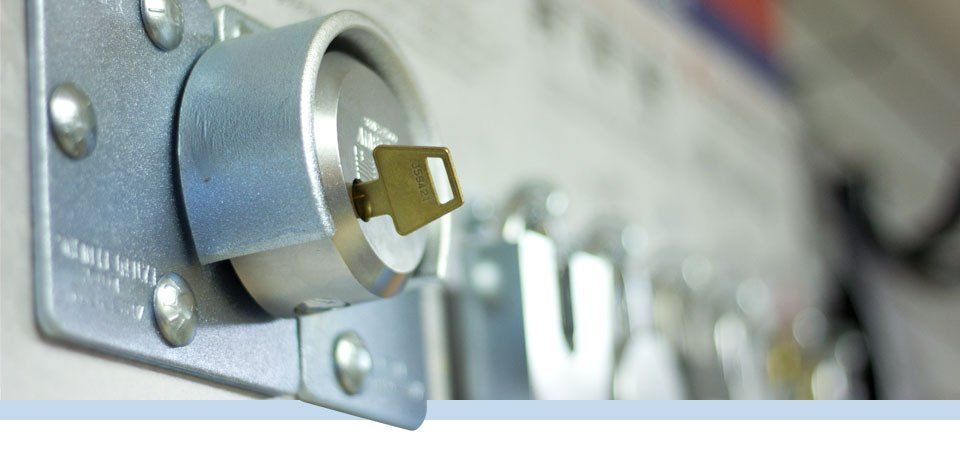 Gros plan sur une clé dans une serrure cylindrique, montée sur une surface métallique, arrière-plan flou avec d'autres serrures.