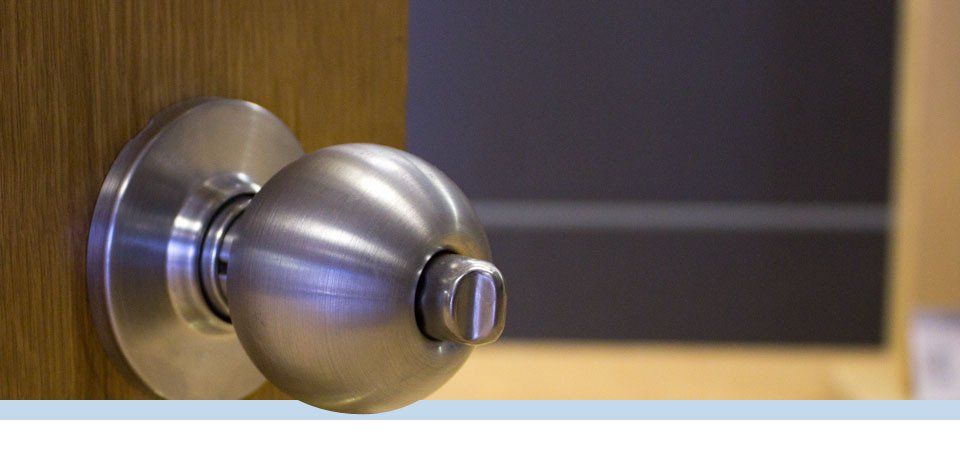 Poignée de porte argentée sur une porte en bois, partiellement ouverte, révélant une pièce sombre.