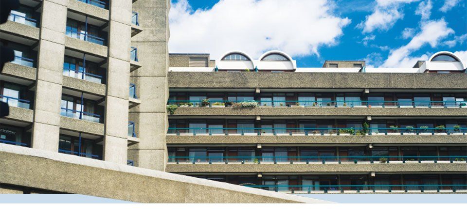Architecture brutaliste moderne, bâtiments en béton avec balcons, sur fond de ciel bleu nuageux.