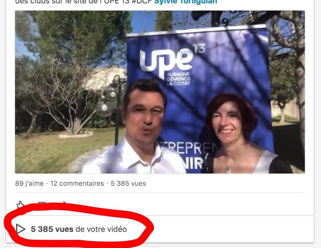 Deux personnes posent à l'extérieur devant un panneau bleu UPE 13, avec un nombre de vues encerclé en dessous.