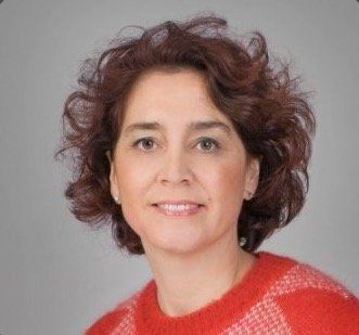 Portrait d'une personne souriante aux cheveux noirs bouclés portant un pull rouge sur fond gris