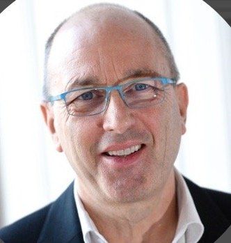 Portrait en gros plan d'un homme souriant portant des lunettes bleues et une veste sombre