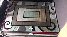 Abstract patterned rug with brown and black geometric border and swirling white accents on a dark floor