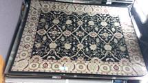 Dark patterned rug with floral border inside a rectangular frame on the floor