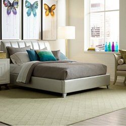 Modern bedroom with gray bed, teal pillows, butterfly wall art, and a window beside a chair and lamp