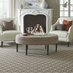 Elegant living room with white fireplace, two armchairs, and a beige ottoman on a patterned rug.
