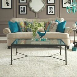 Elegant living room with cream sofa, turquoise pillows, glass coffee table, and teal decor accents