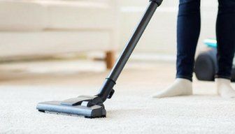 Person vacuuming a light carpet in a bright living room