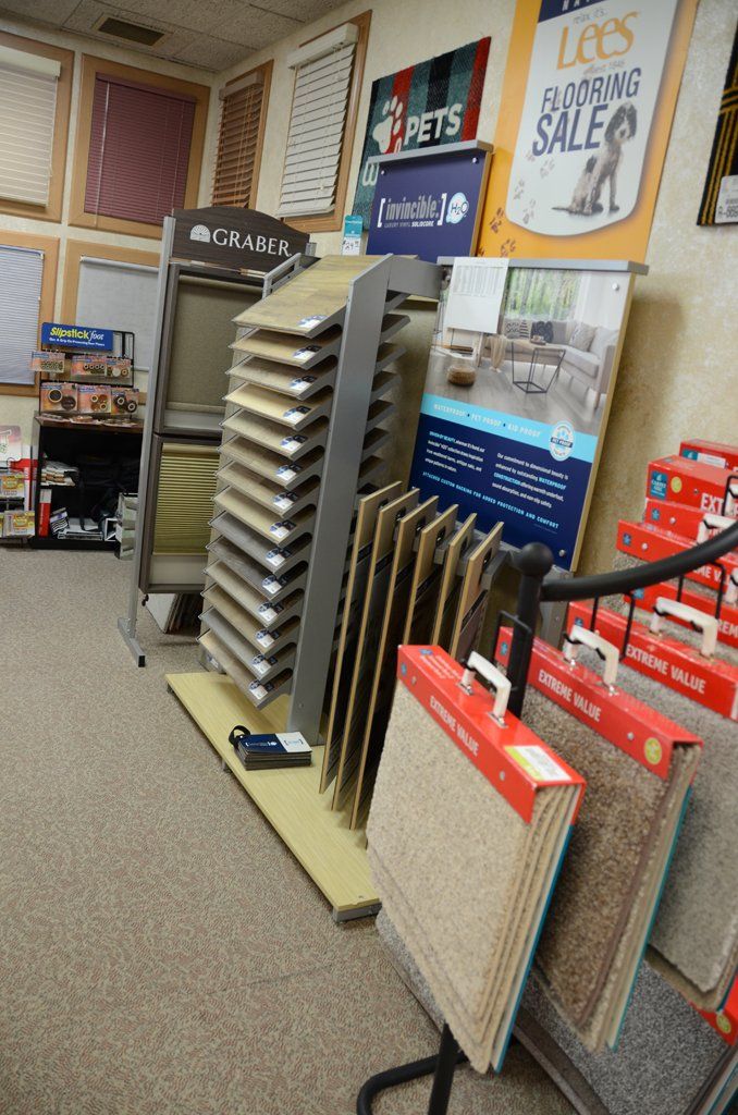 Store showroom displaying flooring samples and carpets on stands, with wall posters in the background