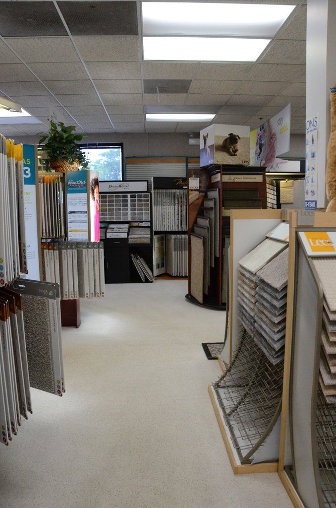 Store aisle with display racks of tiles and flooring samples under fluorescent lights.